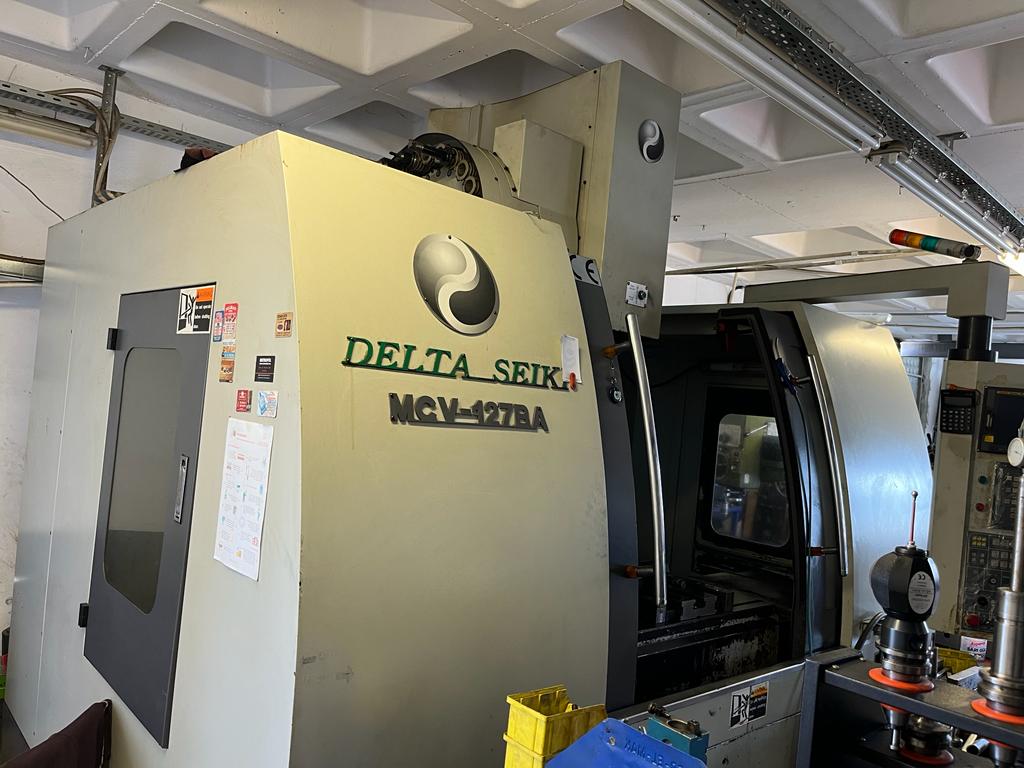 Delta Seiki MCV-127BA CNC Dik İşleme Merkezi Teknolojisi ve Teknik Özellikleri 2 Endüstriyel bir atölyede kurulu durumda olan sarımsı beyaz renkli Delta Seiki MCV-127BA model ağır hizmet tipi döküm gövdeli CNC dik işleme merkezi takım tezgahının dıştan görünümü.